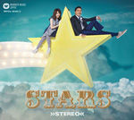 トータス松本とSUPERFLYが大きな星の上に座っているシーン。背景は青空と雲で、星の周囲には明るい照明が施され、楽しい雰囲気を演出している。