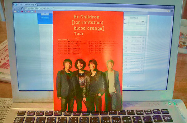 A concert pamphlet for Mr. Children’s '[an imitation] blood orange' tour, displayed on a laptop keyboard.