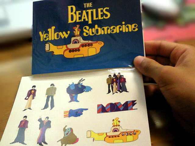 The Beatles 'Yellow Submarine' themed postcard featuring illustrations of the band members and a colorful submarine design.